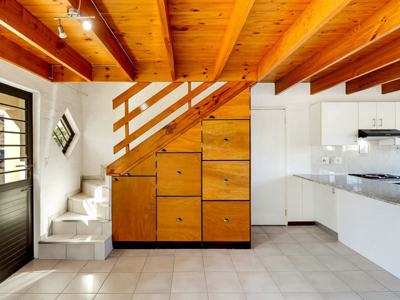 Open-plan living area featuring exposed timber ceiling beams, a custom timber staircase with integrated storage, and a modern kitchen with granite countertops.