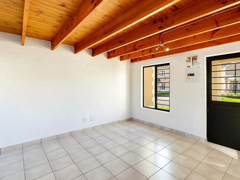 An empty living area featuring exposed timber beam ceilings, tiled flooring, and a secure entrance door with integrated burglar bars.