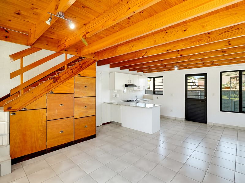 Open-plan living and kitchen area featuring exposed timber beams, tiled flooring, and practical built-in under-stair storage cabinetry.
