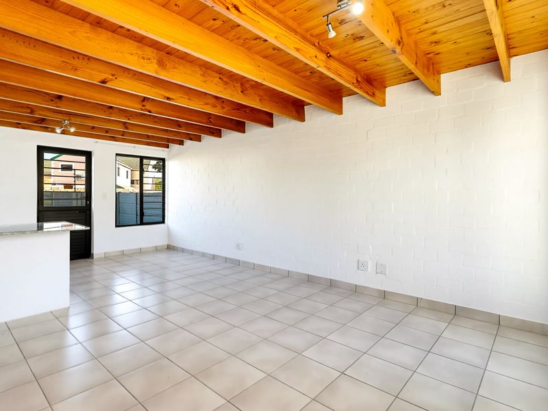 Spacious open-plan living area featuring exposed timber beam ceilings, neutral tiled flooring, and a breakfast nook with granite countertops.