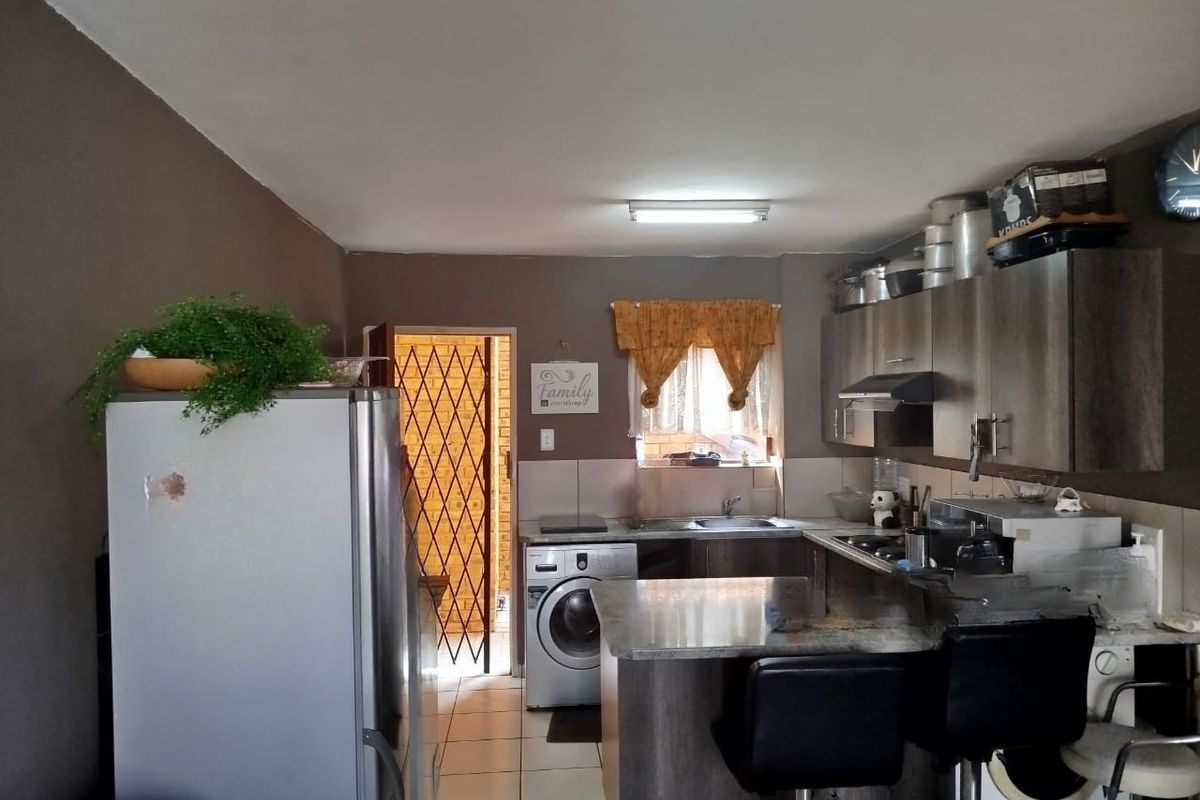 Functional kitchen featuring built-in cabinetry, granite countertops, and tiled flooring, with an adjacent security gate leading to an exterior area.