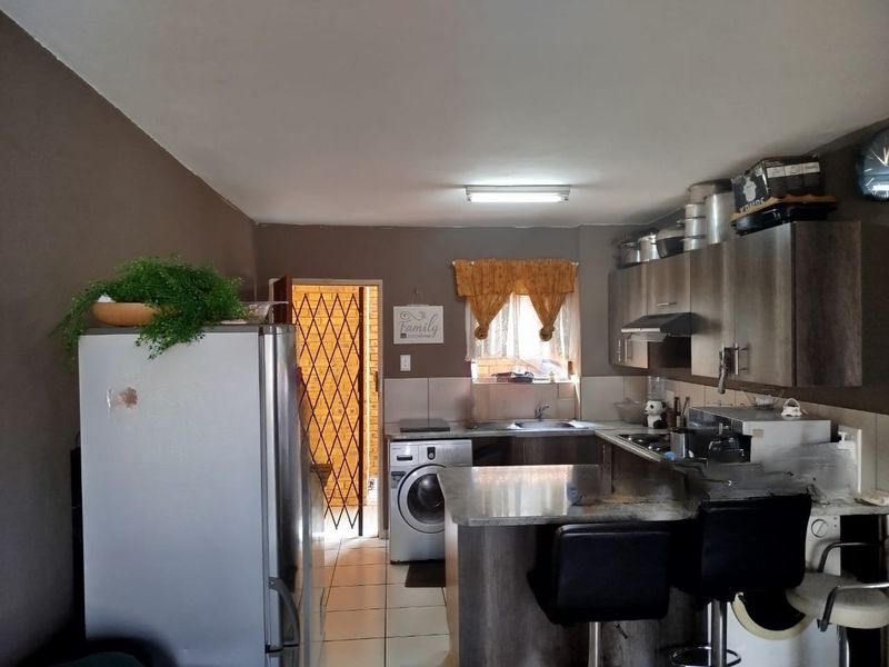 Functional kitchen featuring built-in cabinetry, granite countertops, and tiled flooring, with an adjacent security gate leading to an exterior area.