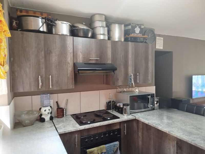 A functional kitchen featuring wood-look cabinetry, stone-effect countertops, a built-in oven with electric hob, and a tiled splashback.