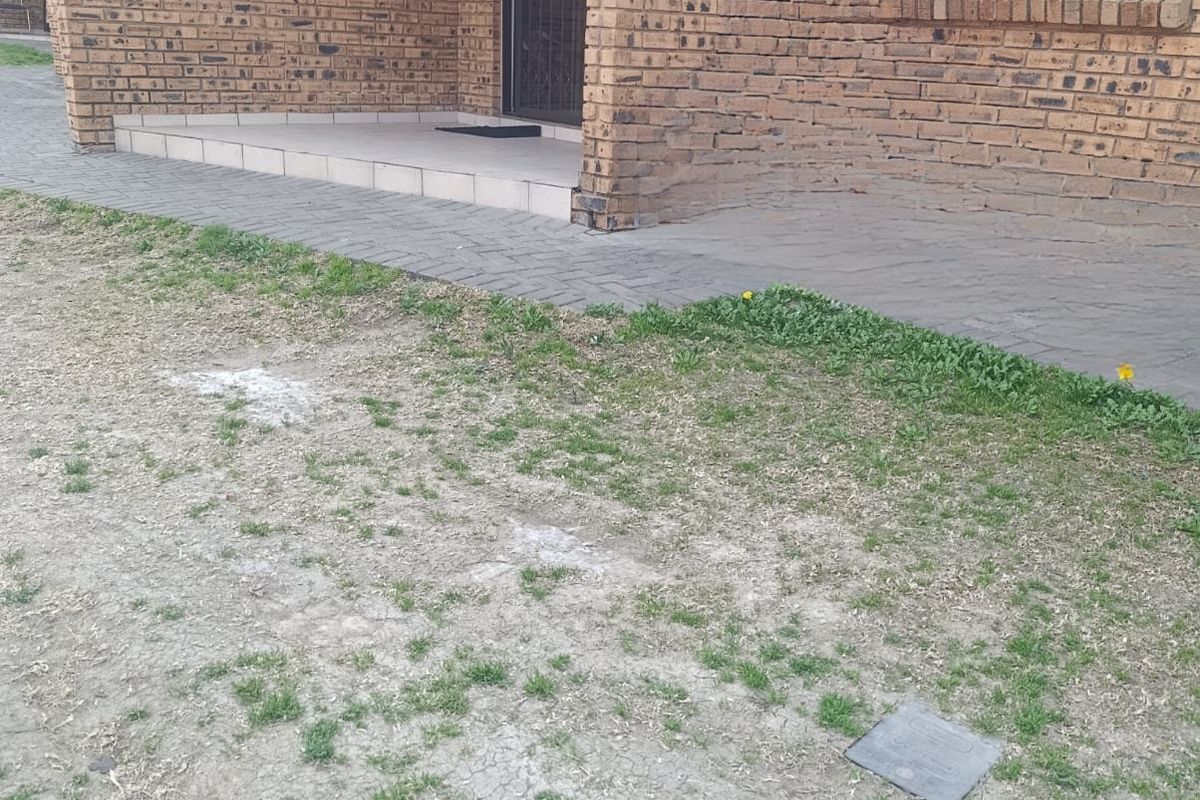 Rear exterior view of a face brick flat featuring a paved patio area and a small garden space.