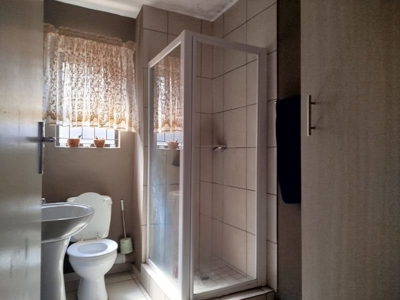 A functional bathroom featuring a pedestal basin, toilet, and a glass-enclosed shower with neutral wall and floor tiling.