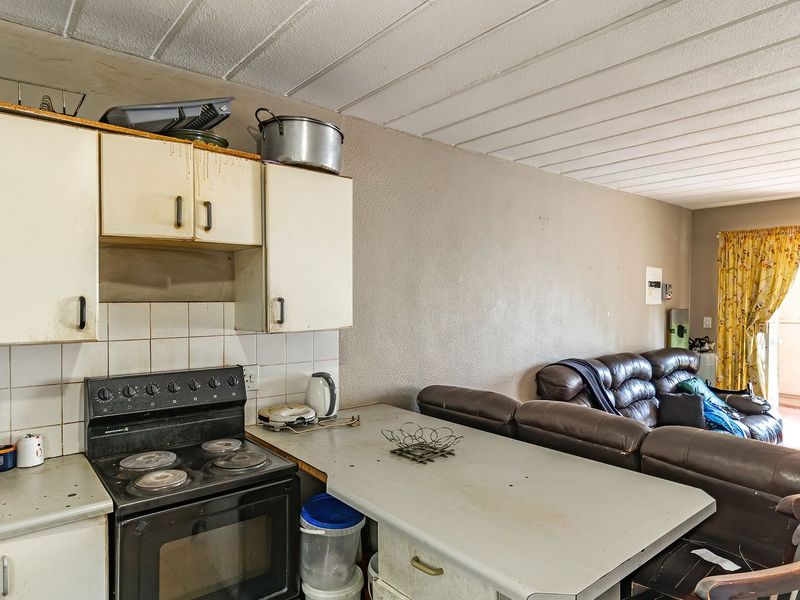 Open-plan kitchen and living area featuring dated cabinetry, a tiled backsplash, and a functional stove, offering potential for modernization and renovation.