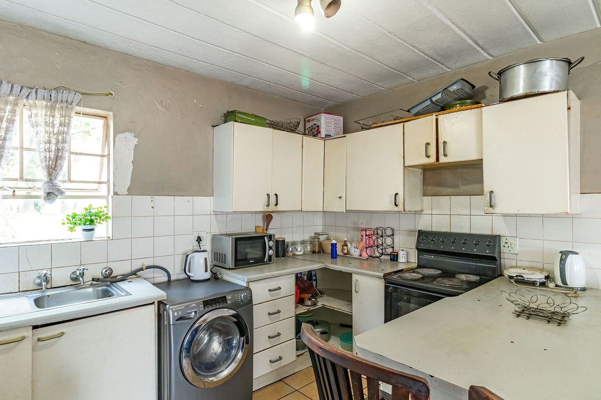 A dated kitchen featuring built-in cabinetry, a stainless steel sink, and an electric stove, requiring cosmetic updates and repairs to wall finishes.
