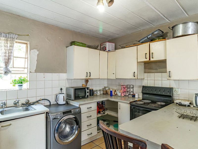 A dated kitchen featuring built-in cabinetry, a stainless steel sink, and an electric stove, requiring cosmetic updates and repairs to wall finishes.