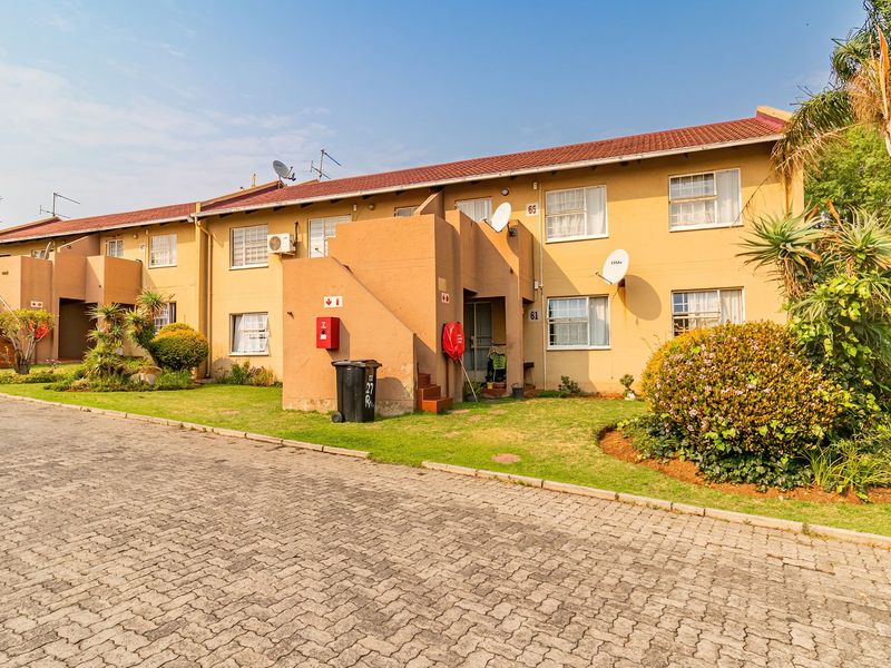 Exterior view of a multi-unit apartment complex featuring a paved driveway, landscaped garden areas, and tiled roofing.