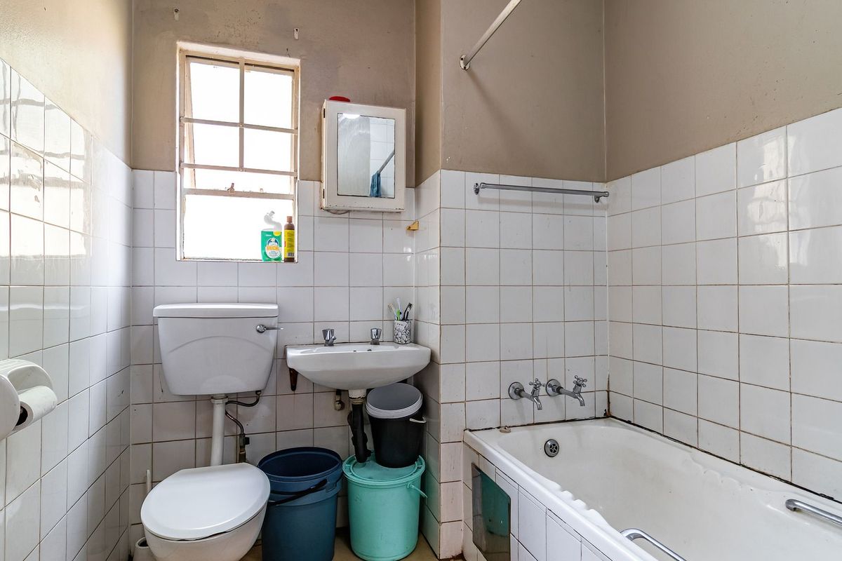 A dated bathroom featuring a standard bathtub, wall-mounted basin, and toilet with white wall tiling and a window for natural light.