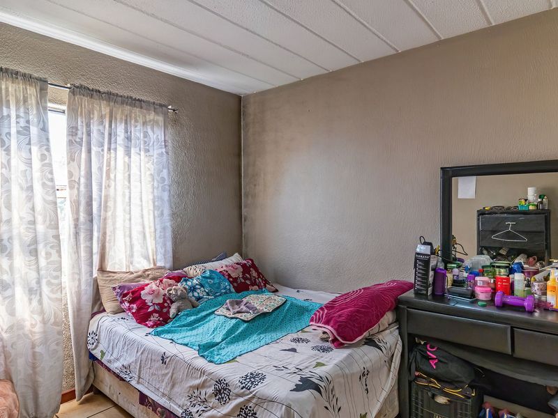 A bedroom featuring a window with curtain rod and textured wall finishes, showing signs of wear and surface staining.