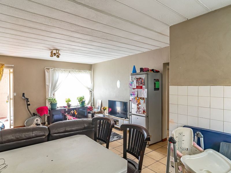 Open-plan living and kitchen area featuring tiled flooring, a tiled kitchen splashback, and textured ceiling panels, offering a functional layout for daily living.