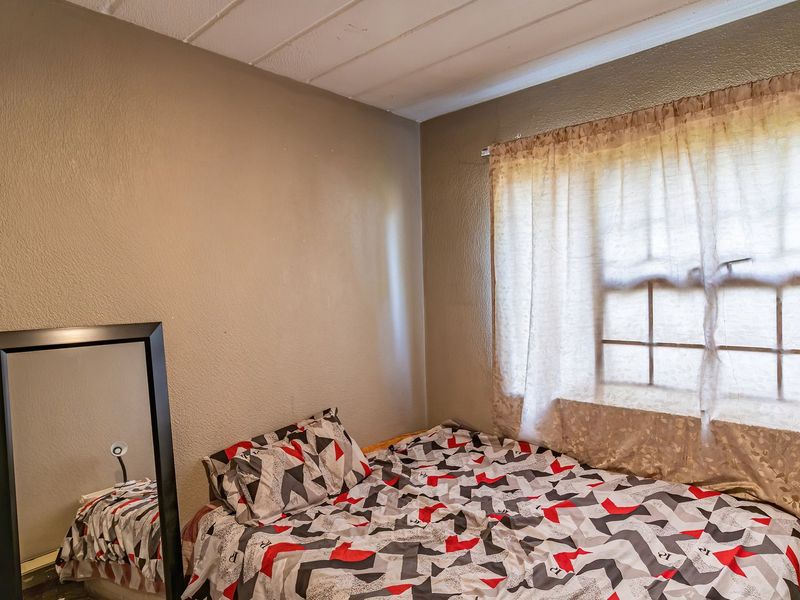 A functional bedroom featuring a window with curtains and a textured ceiling, offering a neutral base for personalization.