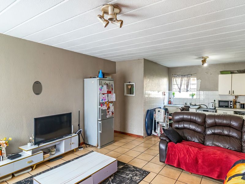 Open-plan living and kitchen area featuring tiled flooring, functional cabinetry, and a tiled backsplash, offering a versatile space for daily living.