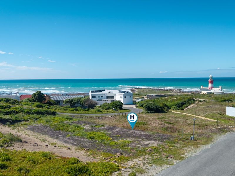 An aerial view of a vacant residential plot situated in a coastal area, featuring proximity to the ocean and a local lighthouse.