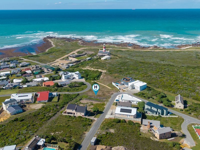 Aerial view of a vacant residential plot situated in a coastal neighborhood, featuring proximity to the ocean and local lighthouse.
