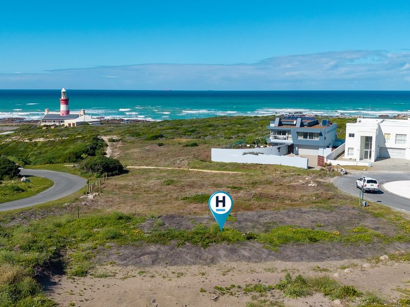 Aerial view of a vacant residential plot situated in a coastal area, featuring proximity to the ocean and local lighthouse.