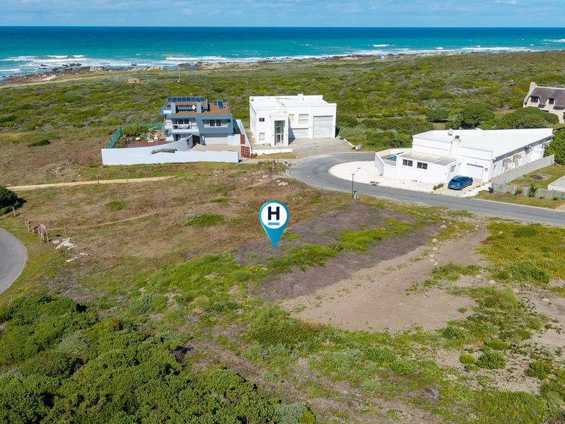 Aerial view of a vacant residential plot situated in a coastal neighborhood with direct road access and proximity to the ocean.