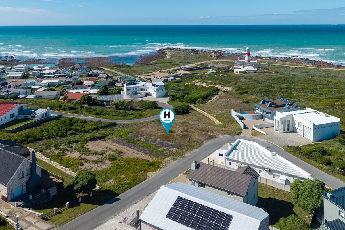 Aerial view of a vacant residential plot situated in a coastal neighborhood, featuring proximity to the ocean and local lighthouse.
