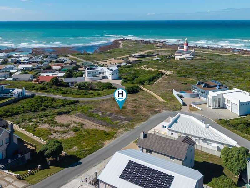 Aerial view of a vacant residential plot situated in a coastal neighborhood, featuring proximity to the ocean and local lighthouse.
