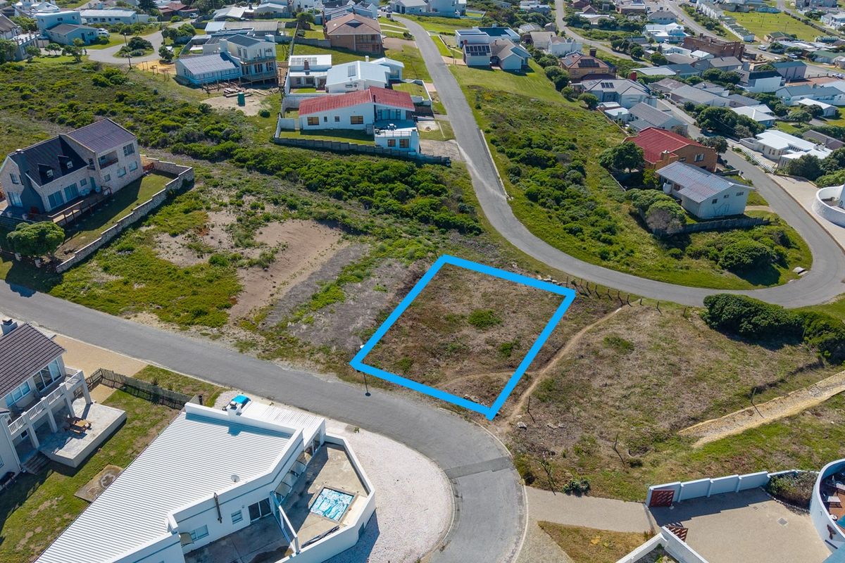 An aerial view of a vacant residential plot situated in a developed coastal neighborhood with established road access.