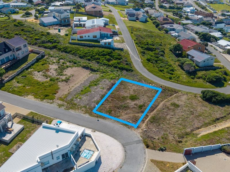 An aerial view of a vacant residential plot situated in a developed coastal neighborhood with established road access.
