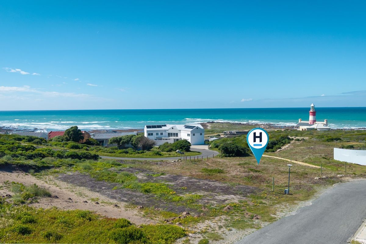 An aerial view of a vacant residential plot situated in a coastal area, featuring proximity to the ocean and a local lighthouse.