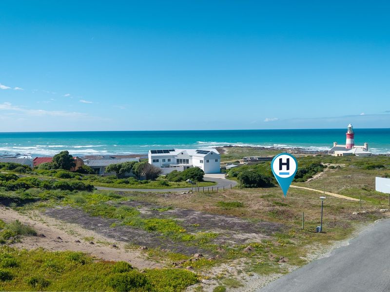 An aerial view of a vacant residential plot situated in a coastal area, featuring proximity to the ocean and a local lighthouse.