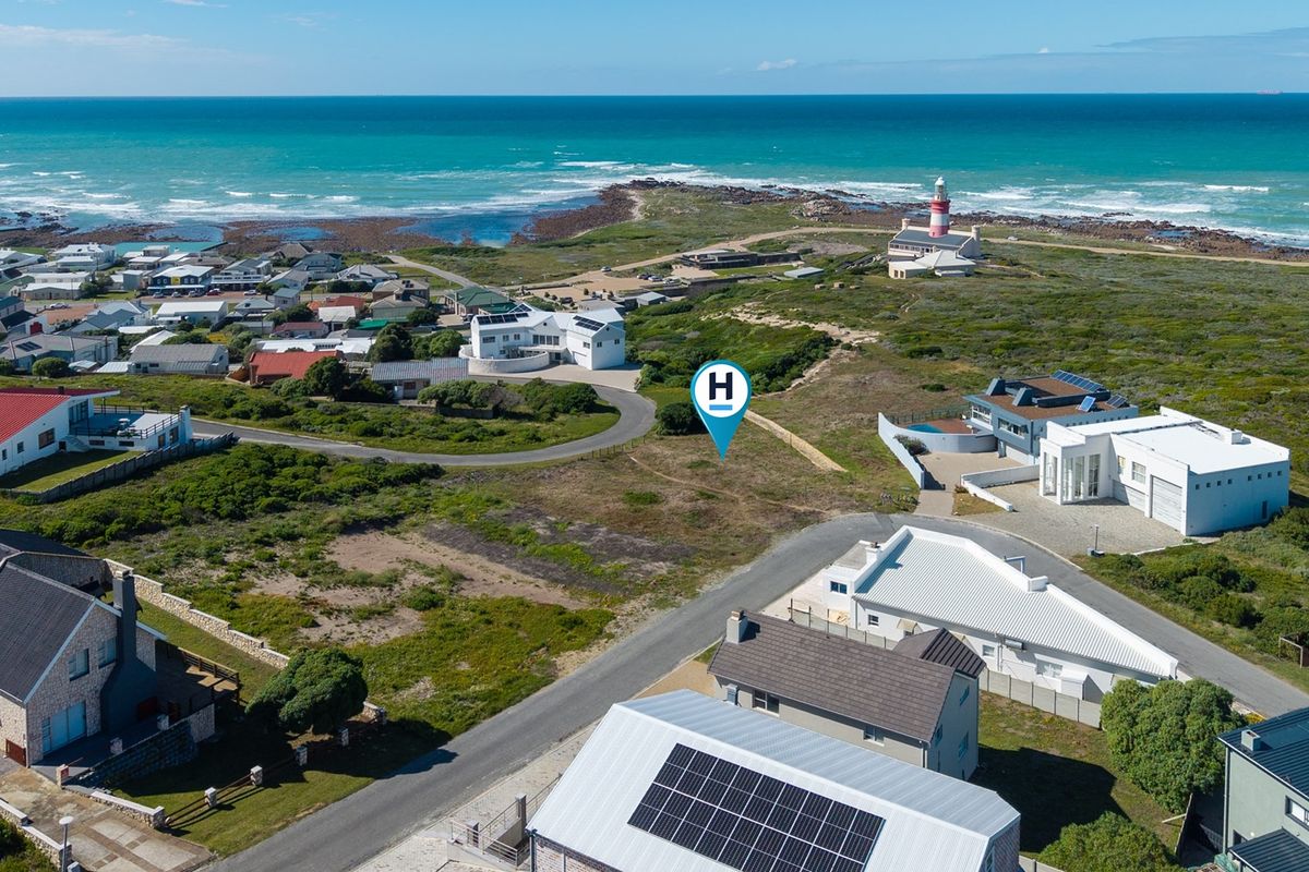 Aerial view of a vacant residential plot situated in a coastal neighborhood, featuring proximity to the ocean and local lighthouse.