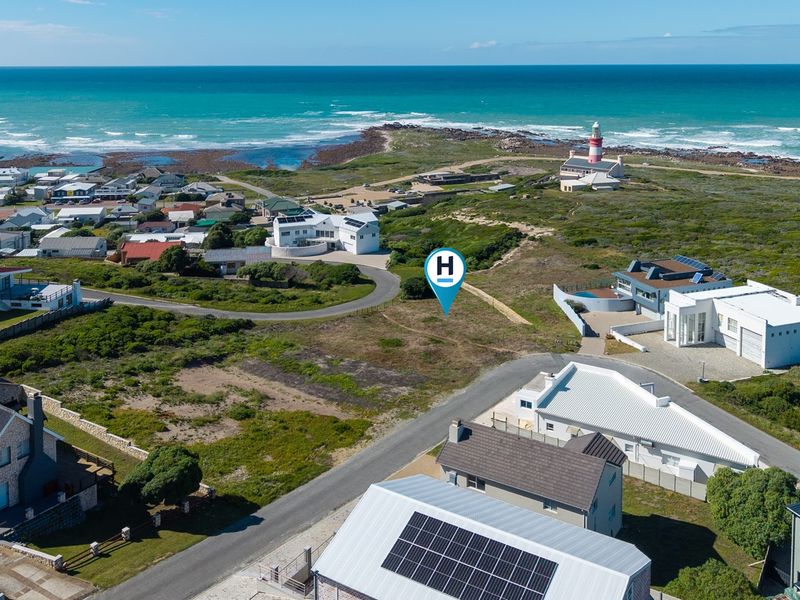 Aerial view of a vacant residential plot situated in a coastal neighborhood, featuring proximity to the ocean and local lighthouse.