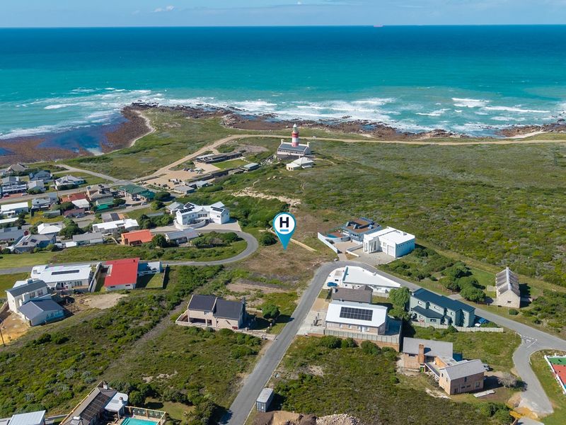 Aerial view of a vacant residential plot situated in a coastal neighborhood, featuring proximity to the ocean and local lighthouse.