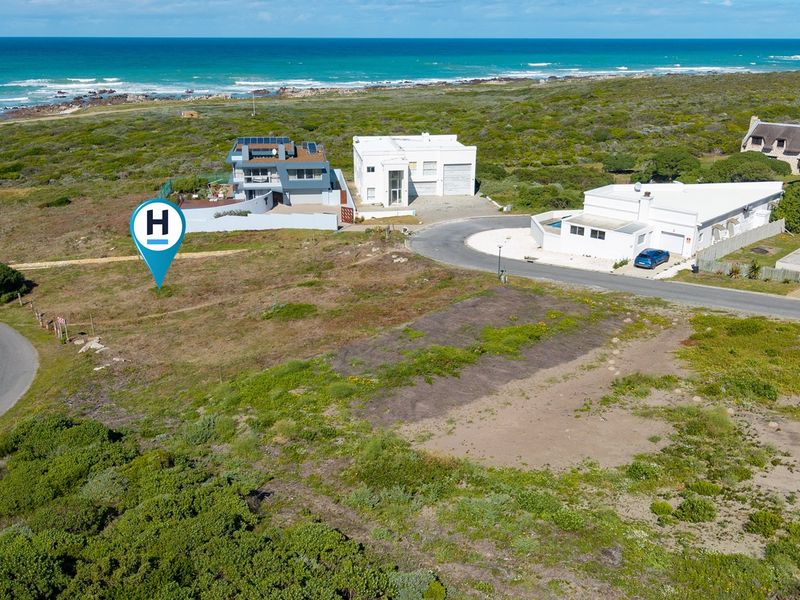 Aerial view of a vacant residential plot situated in a coastal neighborhood with direct road access and proximity to the ocean.