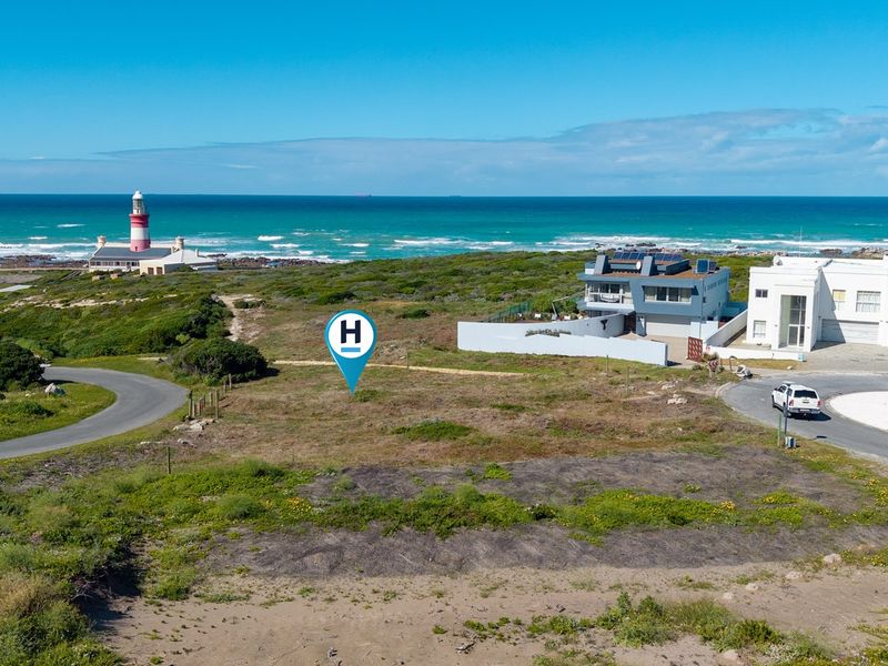 Aerial view of a vacant residential plot situated in a coastal neighborhood, featuring proximity to the ocean and local lighthouse.