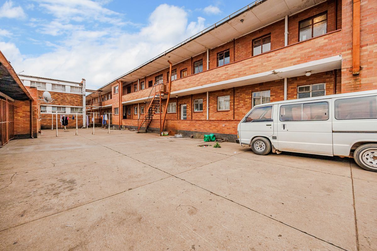 Rear exterior view of a multi-story apartment complex featuring a concrete courtyard, brick facade, and external metal staircase access to upper-level balcony walkways.