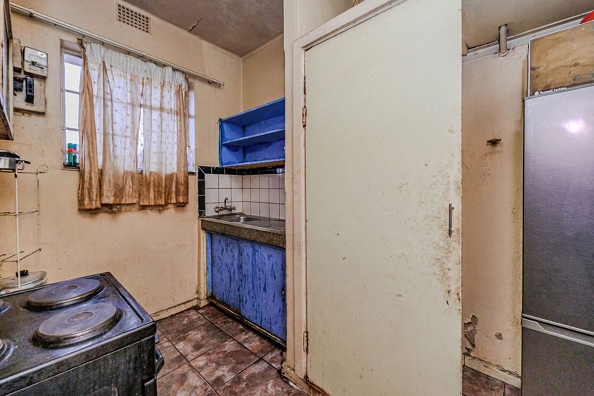 A dated kitchen area featuring original cabinetry, tiled backsplash, and tiled flooring, requiring significant renovation and cosmetic updates to modernize the space.