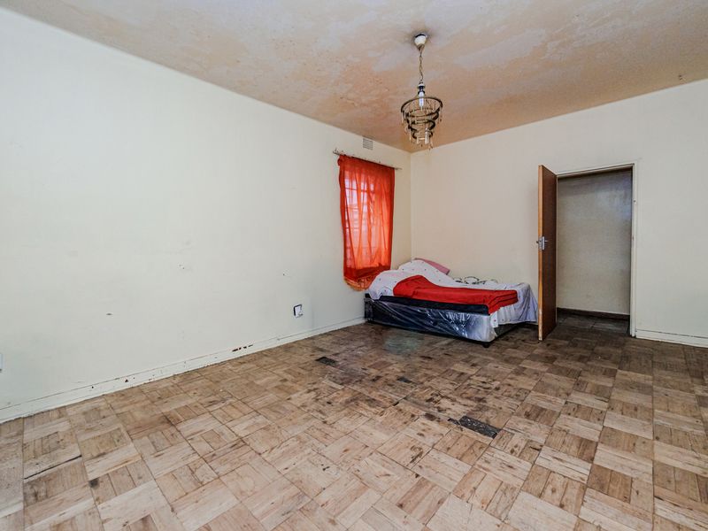 A bedroom featuring original parquet flooring and a ceiling light fixture, requiring cosmetic updates and floor restoration to improve its overall condition.
