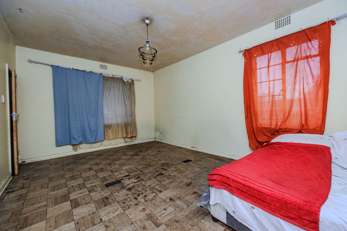 A bedroom featuring original parquet flooring and a ceiling light fixture, requiring cosmetic updates and floor restoration to improve its overall condition.