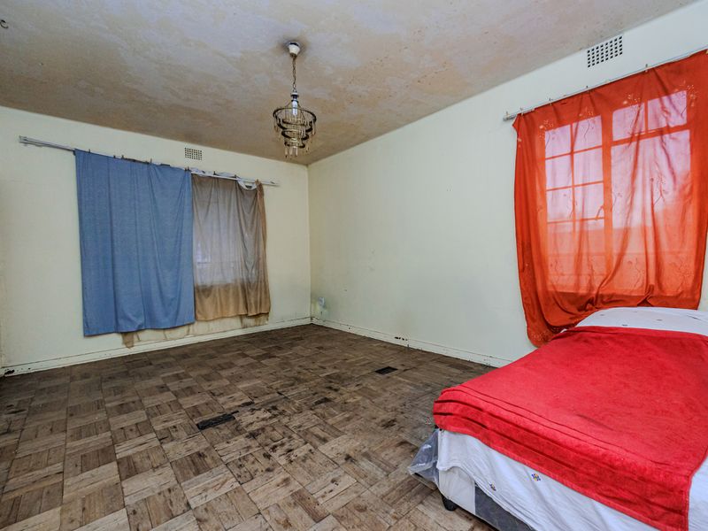 A bedroom featuring original parquet flooring and a ceiling light fixture, requiring cosmetic updates and floor restoration to improve its overall condition.