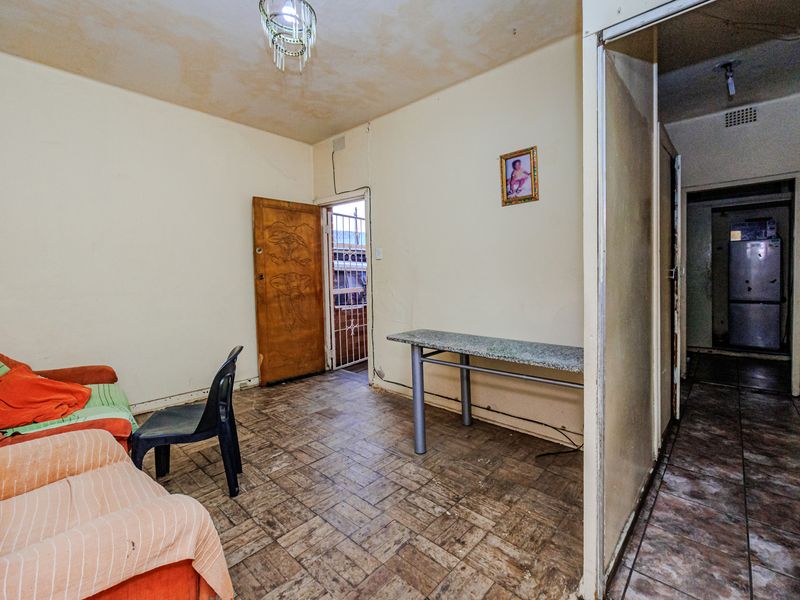 A living area featuring tiled flooring and a security gate, showing signs of wear and requiring cosmetic updates to improve the overall condition.