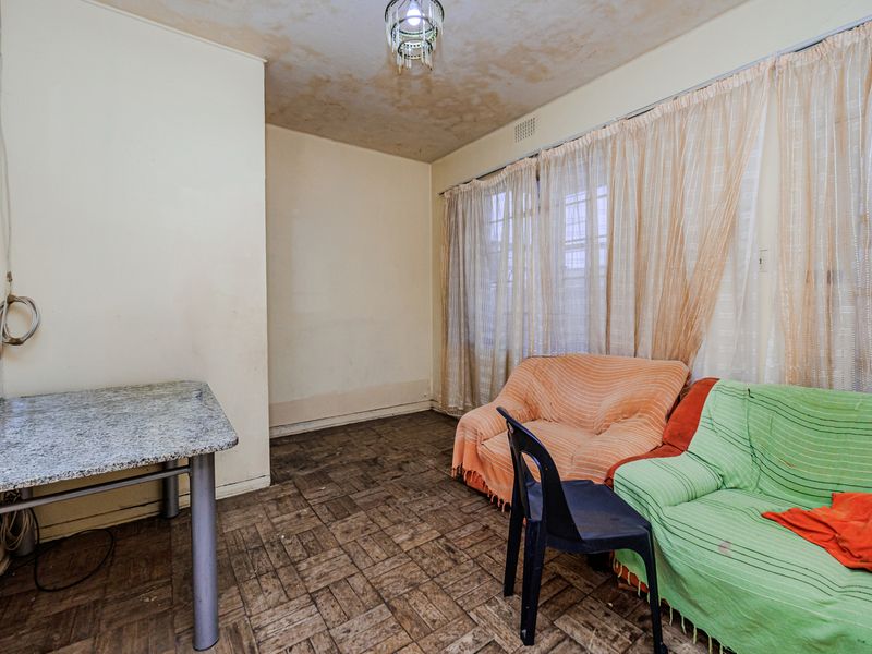 A living room featuring original parquet flooring and a ceiling light fixture, requiring cosmetic updates and ceiling repairs.