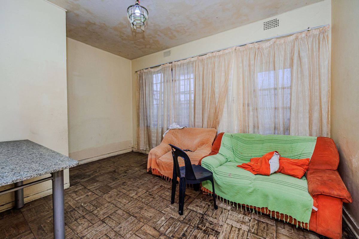 Living room featuring parquet flooring, a built-in breakfast bar, and ceiling ventilation, requiring significant cosmetic updates and repairs to wall and ceiling finishes.
