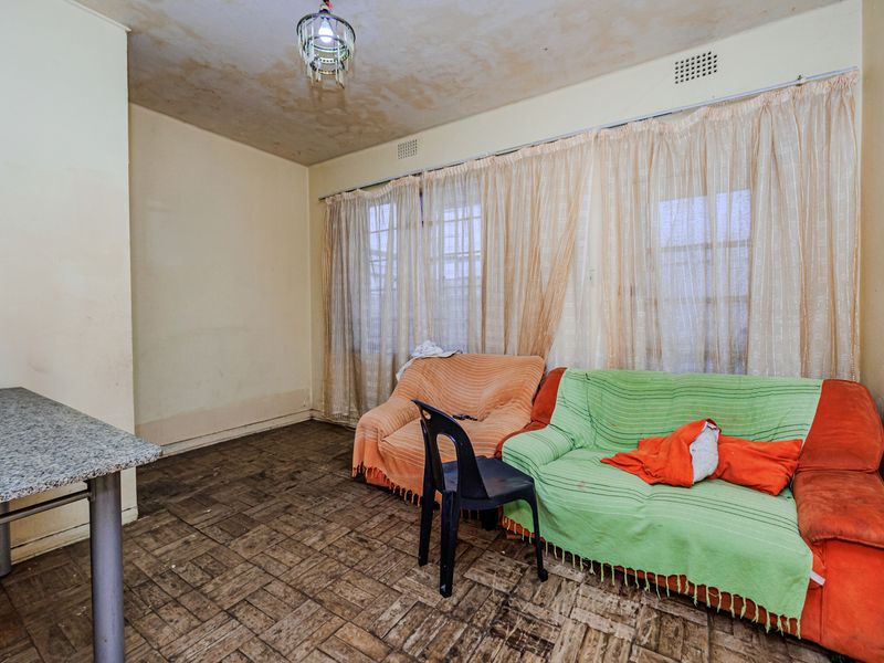 Living room featuring parquet flooring, a built-in breakfast bar, and ceiling ventilation, requiring significant cosmetic updates and repairs to wall and ceiling finishes.