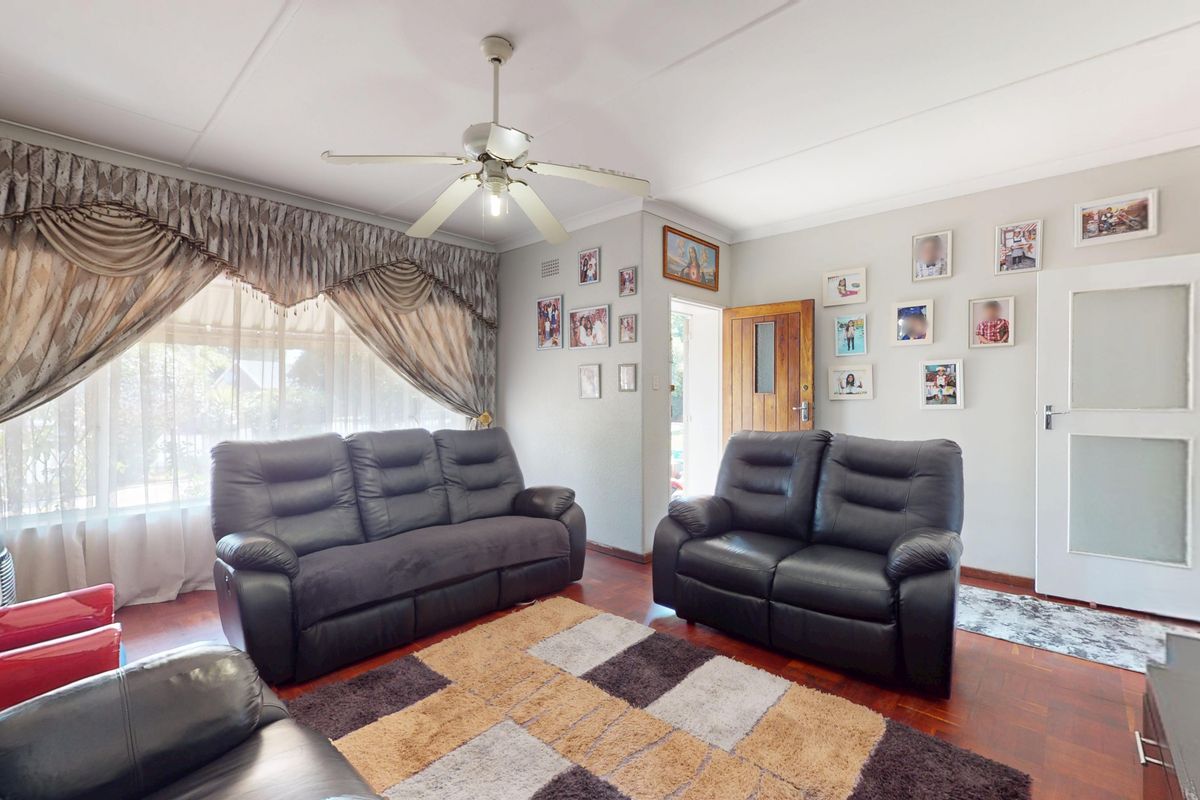 A comfortable living room featuring classic parquet flooring, a ceiling fan, and natural light through large windows.