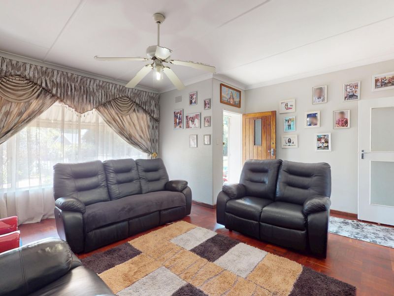 A comfortable living room featuring classic parquet flooring, a ceiling fan, and natural light through large windows.