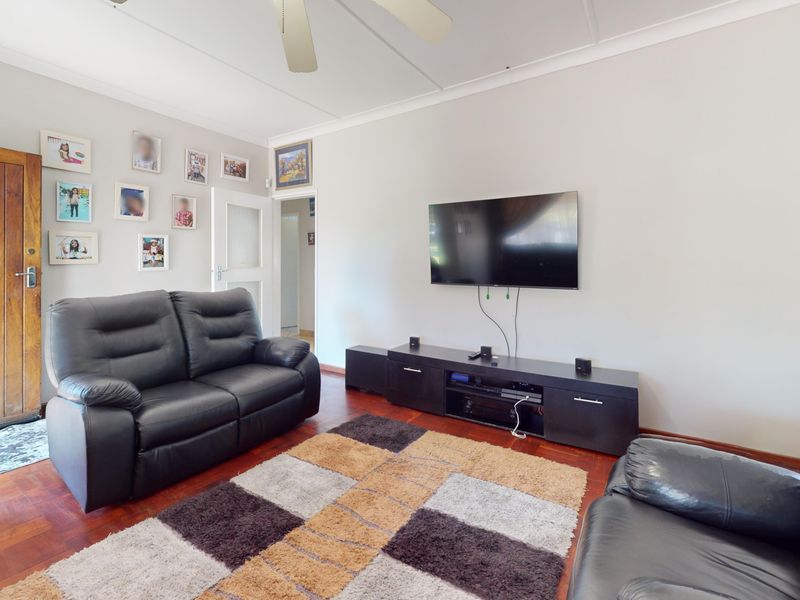 A comfortable living room featuring warm parquet flooring, a ceiling fan, and a solid timber entrance door, creating a welcoming and functional space.
