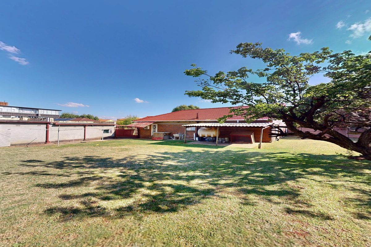 Rear view of the house featuring a spacious lawn, brick facade, tiled roof, and a covered patio area.