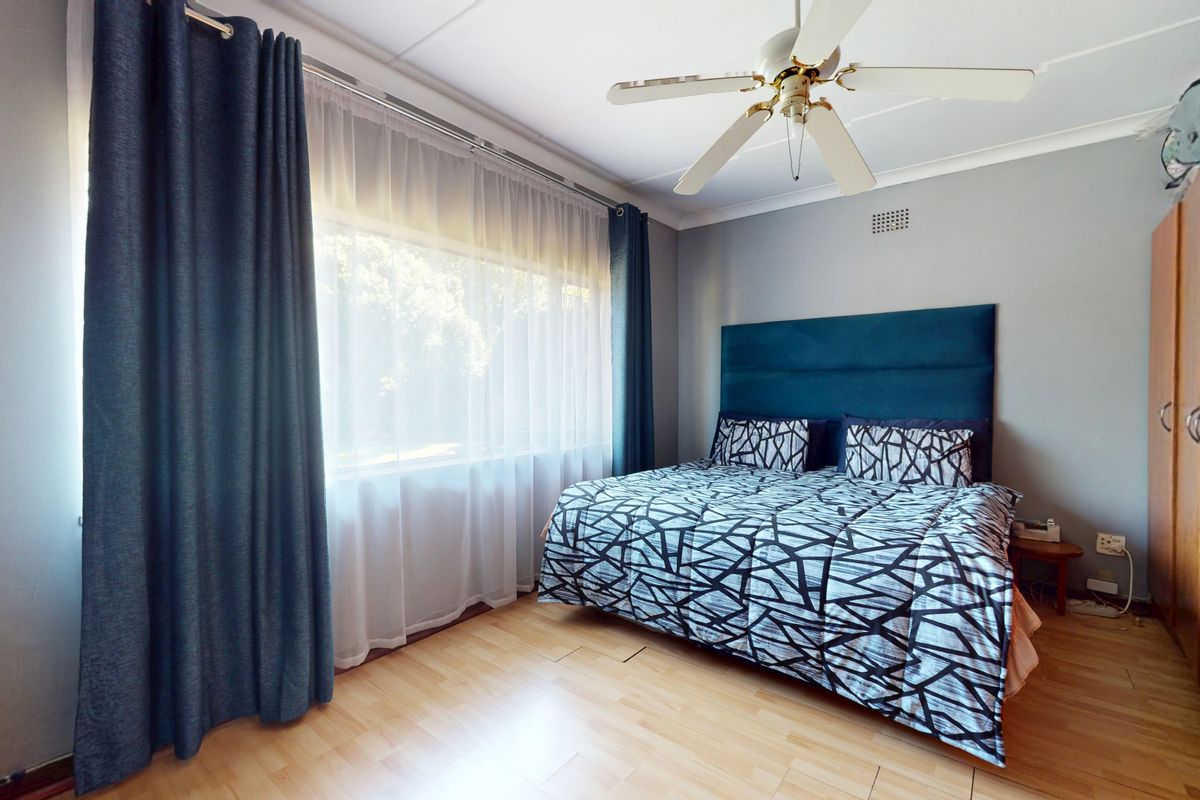 A well-lit bedroom featuring laminate flooring, a ceiling fan, and built-in wardrobe storage, offering a functional and comfortable living space.