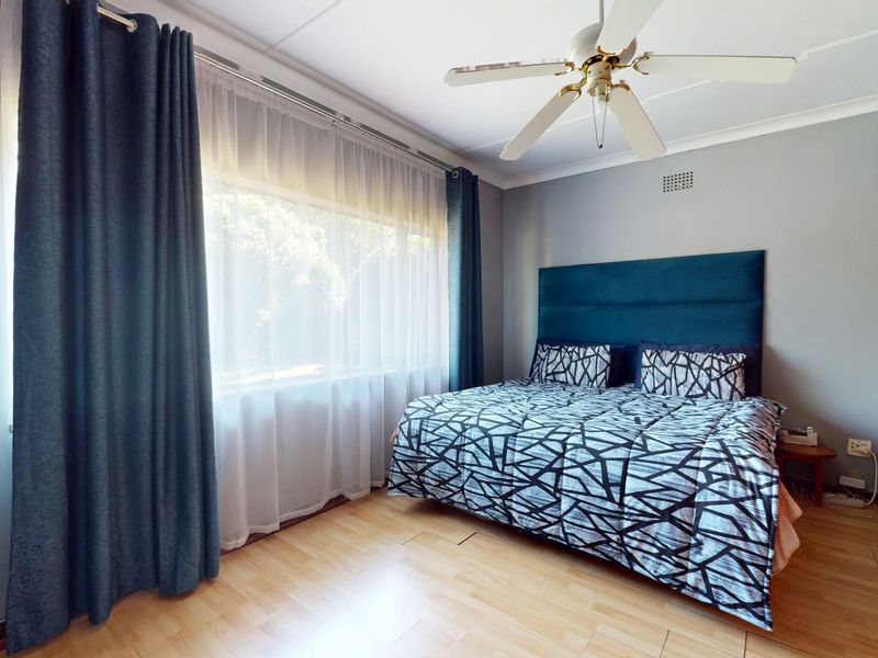 A well-lit bedroom featuring laminate flooring, a ceiling fan, and built-in wardrobe storage, offering a functional and comfortable living space.
