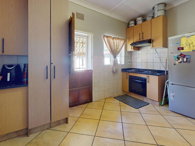 Functional kitchen featuring light wood-finish cabinetry, built-in gas hob and oven, tiled backsplash, and durable floor tiles with direct exterior access.