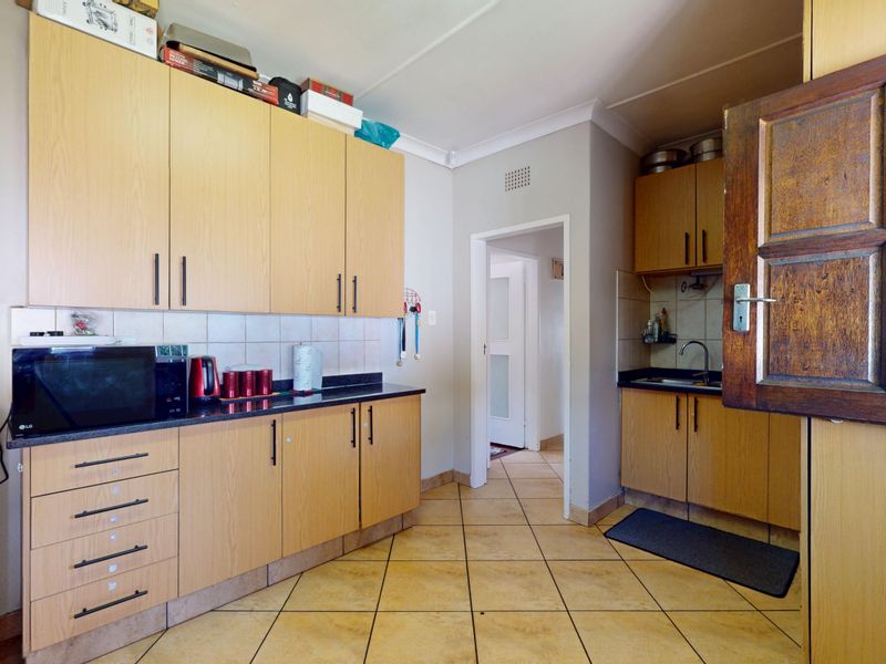 A functional scullery area featuring laminate cabinetry, stone countertops, a stainless steel sink, and tiled flooring.